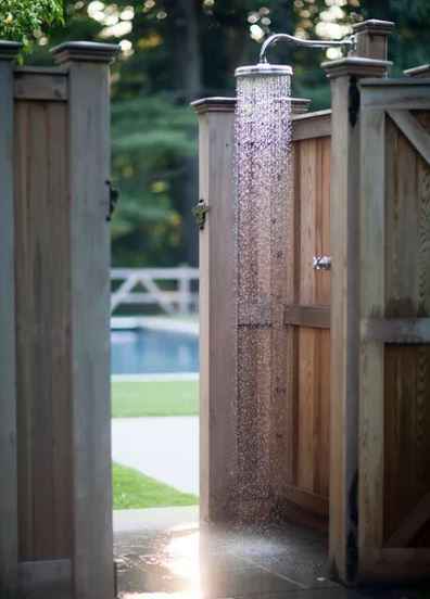 an outdoor shower with wooden doors by a poolside, with water pouring from the showerhead