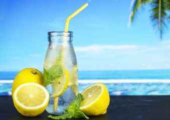 jar of lemonade, in which float lemon and ice, with yellow straw on the bar against an ocean backdrop